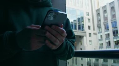 Bir iş adamı ya da bilişim uzmanı elinde bir telefon tutar ve iş merkezinin arka planındaki ortağıyla iletişim kurar.
