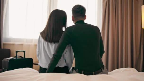 一对年轻夫妇在一间豪华宾馆的房间里 情人坐在床上向窗外望去 — 图库视频影像