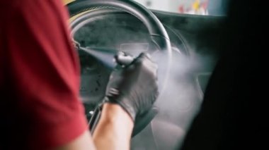 Bir oto yıkama işçisi lüks bir arabanın içini dikkatlice temizler fırça fırçası ve elektrikli süpürgeyle temizler.