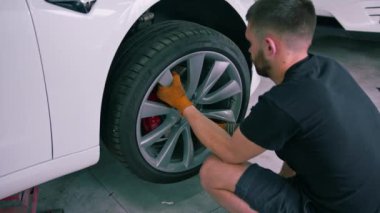 Otomotiv tamircisi, lüks beyaz bir arabanın tekerleğini değiştiriyor. Yakından çekilen bir araba servisinde balon anahtarı kullanıyor.