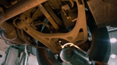 Elinde el feneri olan erkek tamirci arabanın tabanını inceler ve arabanın süspansiyonunda arıza arar.