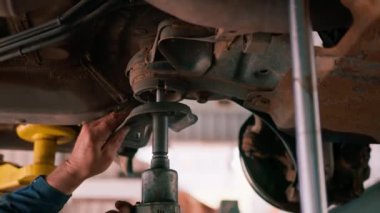 Yakın plan erkek araba servisi çalışanı, İngiliz anahtarı ve tornavida kullanarak lüks bir arabanın süspansiyonunu tamir ediyor.