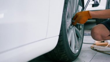Otomotiv tamircisi, lüks beyaz bir arabanın tekerleğini değiştiriyor. Yakından çekilen bir araba servisinde balon anahtarı kullanıyor.
