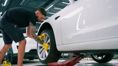 Otomotiv tamircisi, lüks beyaz bir arabanın tekerleğini değiştiriyor. Yakından çekilen bir araba servisinde balon anahtarı kullanıyor.