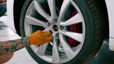 Otomotiv tamircisi, lüks beyaz bir arabanın tekerleğini değiştiriyor. Yakından çekilen bir araba servisinde balon anahtarı kullanıyor.