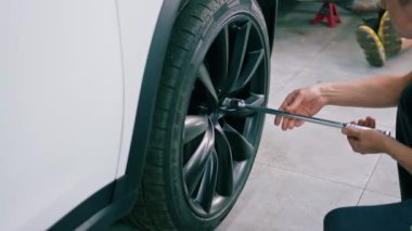 Otomotiv tamircisi, lüks beyaz bir arabanın tekerleğini değiştiriyor. Yakından çekilen bir araba servisinde balon anahtarı kullanıyor.