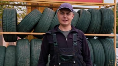 Ciddi bir oto tamircisinin portresi elinde silindir anahtarla başparmak sinyalini gösteriyor. Arka planda araba lastiği tamiri var.