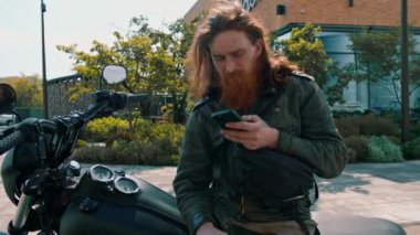 Vahşi, düşünceli, kızıl sakallı motosikletli, siyah motosikletli, elinde telefonla hız yarışından sonra elinde bir portre.