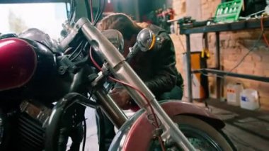 Yaratıcı otantik motosiklet atölyesi. Motorcu garajındaki sakallı, sakallı tamirci. Motosiklet, kabloları bıçakla temizliyor.