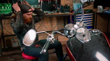 Yaratıcı otantik motosiklet atölyesi kızıl saçlı sakallı tamirci motorcu garajında motosiklet aletlerini tamir ediyor.
