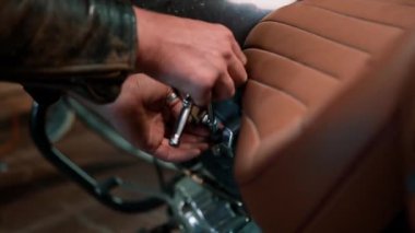 Yaratıcı otantik motosiklet atölyesi kızıl saçlı sakallı tamirci motosiklet garajında motosiklet koltuğunu tamir ederken yakın çekim aletleri kullanıyor.