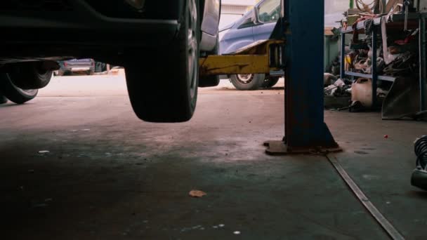 車のサービス労働者は車を点検し 修理するために青い上昇の贅沢な灰色の車を持ち上げます — ストック動画
