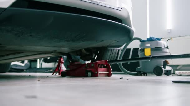 詳細とドライクリーニング中に車サービスで赤いホイールチェンジジャックで持ち上げられたホワイト高級車 — ストック動画