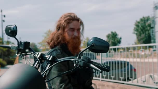 レースラストスピードモータースポーツコンセプトの後に黒いオートバイに座って思慮深い赤毛のひげを笑顔の肖像画 — ストック動画