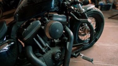 Tamirhanedeki bir tamirci atölyesinde duran siyah, güzel bir motorsikletin ayrıntılarına yakın plan.