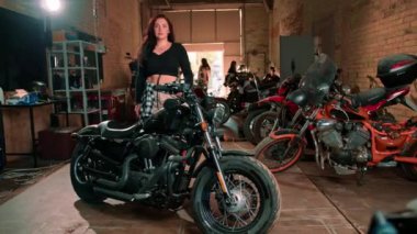 Otantik motosiklet atölyesi güzel genç motorcu kız havalı siyah motosikletin yanında duruyor.