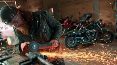 Yaratıcı otantik motosiklet atölyesi kızıl saçlı, sakallı, vahşi motosikletli, dairesel testere ile sıcak metalden kıvılcımlar uçuşuyor.
