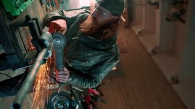 Yaratıcı otantik motosiklet atölyesi kızıl sakallı, vahşi motosikletli, dairesel testereli Sparks, sıcak metal dikey video kasetinden uçuyor.