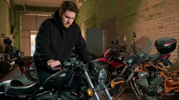 摩托车修理厂站在摩托车检测台旁 大胡子骑黑色连帽衫自行车的人 — 图库视频影像