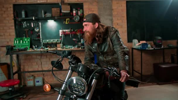创意正宗的摩托车车间车库肖像画严肃的红头发摩托技师坐摩托车 — 图库视频影像