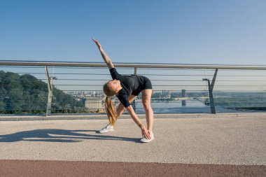 Fitness genç sporcu kız sabah ısınma egzersizleri yapıyor. Şehirdeki köprüdeki spor salonunda antrenmandan önce.