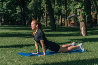 Genç sporcu kız spor minderi üzerinde fiziksel egzersiz yapıyor. Yoga eğitimi alıyor. Parkta çimenler üzerinde sağlıklı yaşam tarzı konsepti.