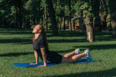 Genç sporcu kız spor minderi üzerinde fiziksel egzersiz yapıyor. Yoga eğitimi alıyor. Parkta çimenler üzerinde sağlıklı yaşam tarzı konsepti.