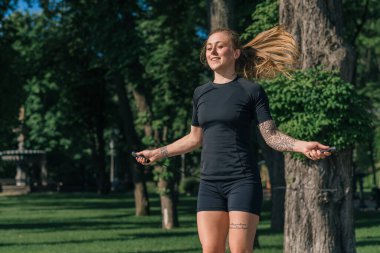 Spor salonundaki sporcu kız, sabah dövmeli, spor atlama halatı yapıyor, şehirde sağlık parkında egzersiz yapıyor.
