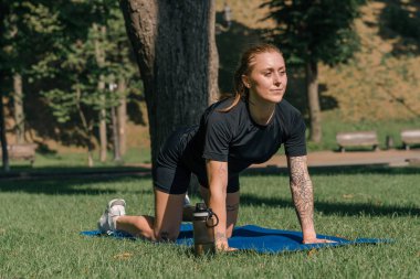 Genç sporcu kız spor minderi üzerinde fiziksel egzersiz yapıyor. Yoga eğitimi alıyor. Parkta çimenler üzerinde sağlıklı yaşam tarzı konsepti.