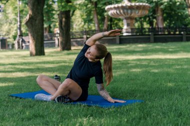Genç sporcu kız spor minderi üzerinde fiziksel egzersiz yapıyor. Yoga eğitimi alıyor. Parkta çimenler üzerinde sağlıklı yaşam tarzı konsepti.