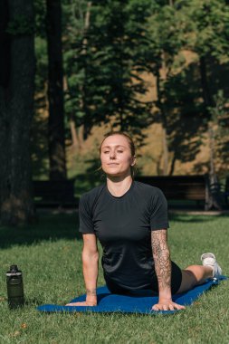 Genç sporcu kız spor minderi üzerinde fiziksel egzersiz yapıyor. Yoga eğitimi alıyor. Parkta çimenler üzerinde sağlıklı yaşam tarzı konsepti.