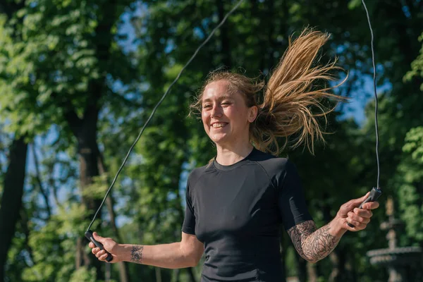 ポートレートフィットネス若い笑顔スポーツウーマン少女は ヘルスパークの郊外で運動中にスポーツジャンプロープをしている — ストック写真