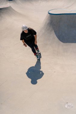 Genç yetenekli kadın paten kayıyor ve dışarıdaki kaykay parkında rampada zıplıyor. Numaralarını ya da paten yarışması tekniğini deniyor.
