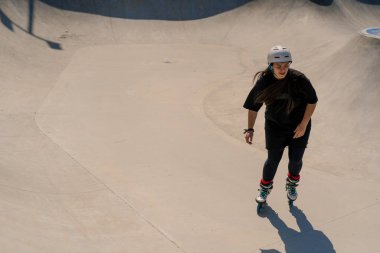Genç yetenekli kadın paten kayıyor ve dışarıdaki kaykay parkında rampada zıplıyor. Numaralarını ya da paten yarışması tekniğini deniyor.