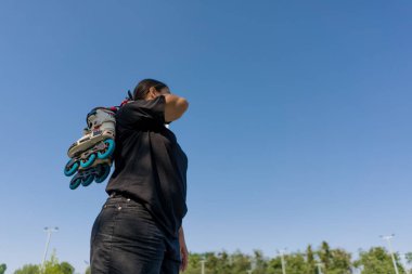 Genç hippi kız antrenmanlara başlamadan önce paten taşıyor. Spor sahasında sokak sporu.