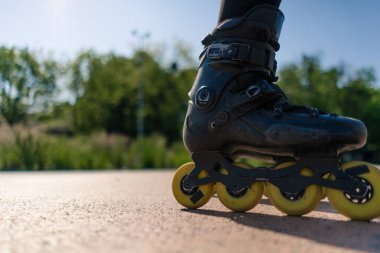 Parkın arka planında paten kayan sporcu kız. Paten dersinin tadını çıkarıyor. Ayaklarını yakın tut, sokak sporu.