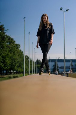 Parkın arka planında paten kayan sporcu kız. Paten dersinin tadını çıkarıyor. Ayaklarını yakın tut, sokak sporu.