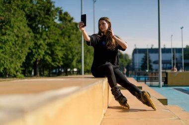 Spor sahasında paten kayan sporcu kız, dersten memnun, telefon caddesinde aktif spor yaşam tarzında kendi fotoğrafını çekiyor.