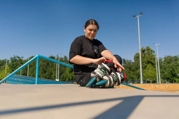 ローラースケートでスケートパークに座っている若いヒップスター少女は トレーニングを開始する前にスポーツグラウンドストリートスポーツを閉じます — ストック写真