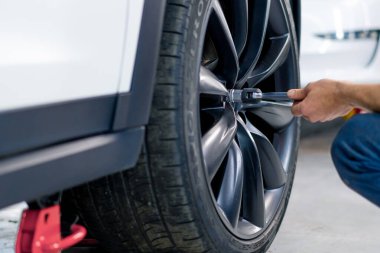 Otomotiv tamircisi, lüks beyaz bir arabanın tekerleğini değiştiriyor. Yakından çekilen bir araba servisinde balon anahtarı kullanıyor.