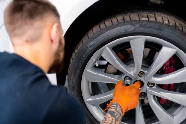 Otomotiv tamircisi, lüks beyaz bir arabanın tekerleğini değiştiriyor. Yakından çekilen bir araba servisinde balon anahtarı kullanıyor.