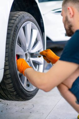 Otomotiv tamircisi, lüks beyaz bir arabanın tekerleğini değiştiriyor. Yakından çekilen bir araba servisinde balon anahtarı kullanıyor.