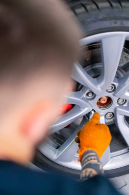 Otomobil tamircisi, lüks beyaz bir arabanın tekerini değiştiriyor. Arkasından bir araba servis istasyonunda balon anahtarı kullanıyor.