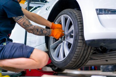 Otomotiv tamircisi, lüks beyaz bir arabanın tekerleğini değiştiriyor. Yakından çekilen bir araba servisinde balon anahtarı kullanıyor.