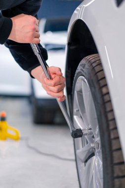 Otomotiv tamircisi, lüks beyaz bir arabanın tekerleğini değiştiriyor. Yakından çekilen bir araba servisinde balon anahtarı kullanıyor.