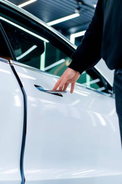 Bir adam araba servisinde kuru temizleme ve temizlik yaptıktan sonra lüks beyaz arabasının kapısını açar.