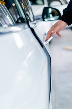 Bir adam araba servisinde kuru temizleme ve temizlik yaptıktan sonra lüks beyaz arabasının kapısını açar.