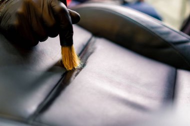 Bir oto yıkama işçisi lüks bir arabanın içini dikkatlice temizler fırça fırçası ve elektrikli süpürgeyle yakın plan temizlik yapar.