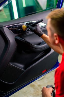 Bir oto yıkama işçisi lüks bir arabanın içini dikkatlice temizler fırça fırçası ve elektrikli süpürgeyle yakın plan temizlik yapar.
