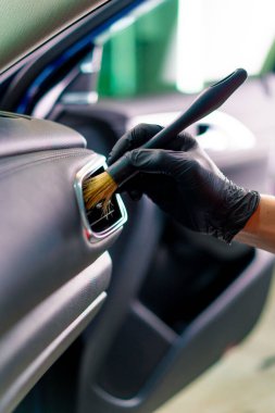 Bir oto yıkama işçisi lüks bir arabanın içini dikkatlice temizler fırça fırçası ve elektrikli süpürgeyle yakın plan temizlik yapar.